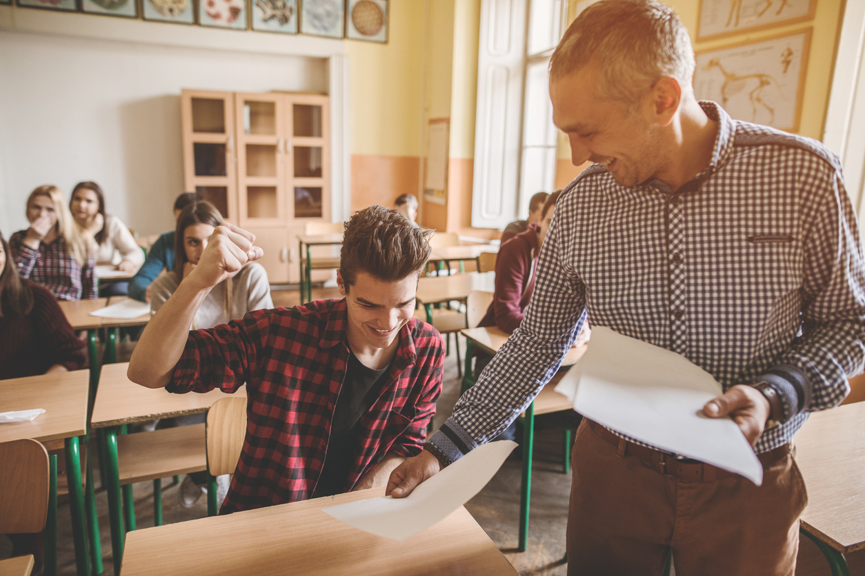 How to Figure Out Your GPA and Why It Matters Student pumping his fist as he gets a good test score back from a teacher.