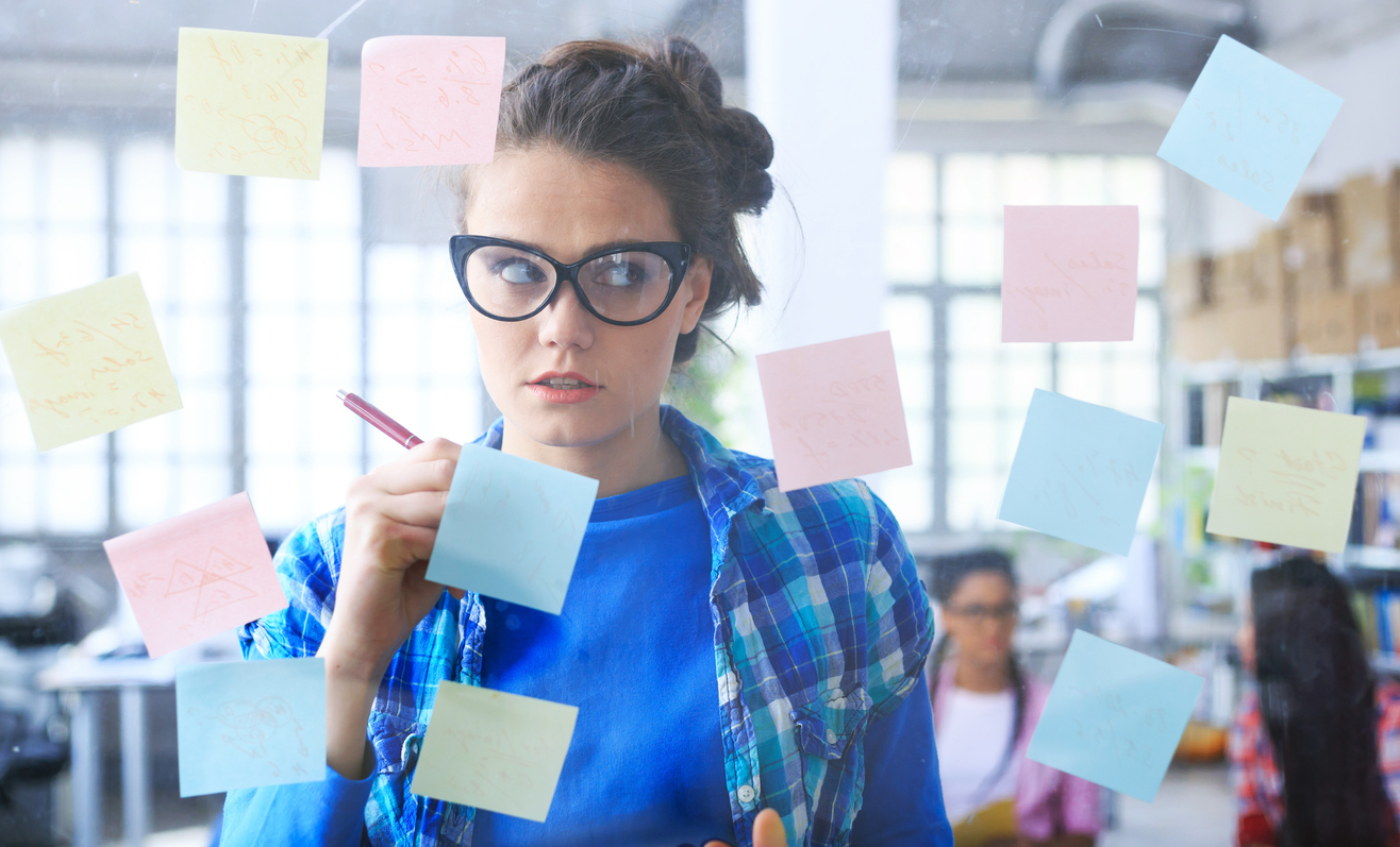 What (Not) to Write About in Your College Essay Young woman looking confused at post-it notes on a glass wall.